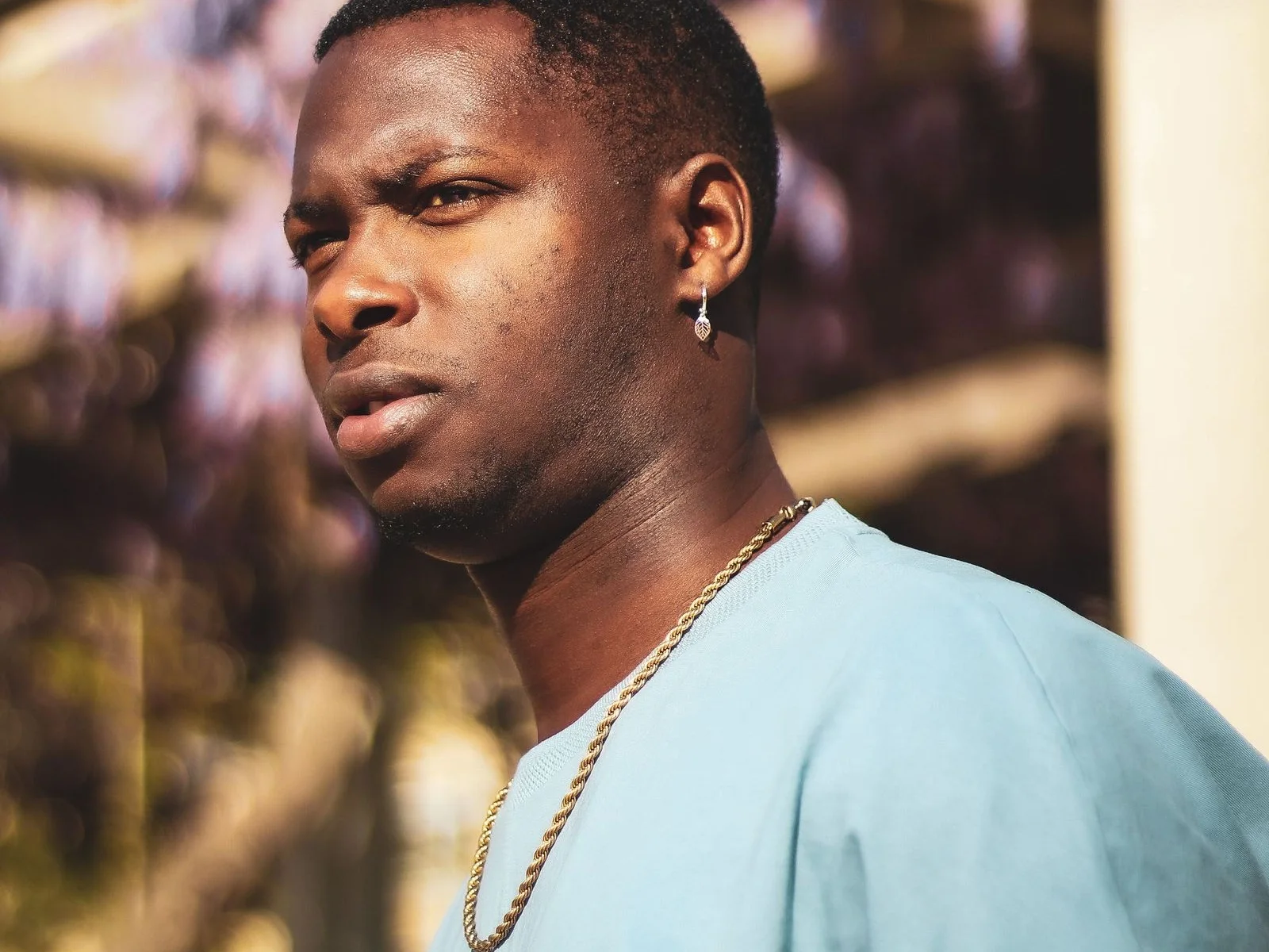 Man outdoors in a light blue T-shirt wearing a gold rope chain and a small drop earring