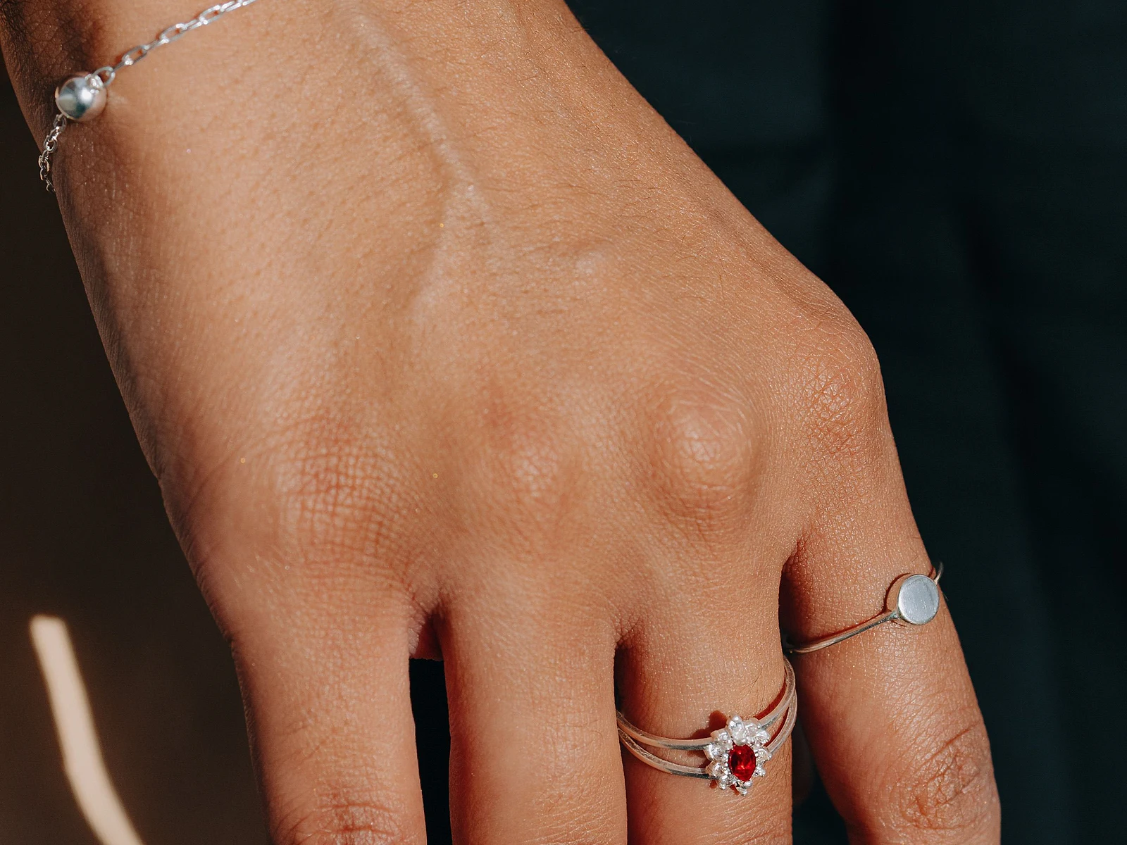 Hand with a fine silver bracelet and two delicate silver rings against a tailored blazer