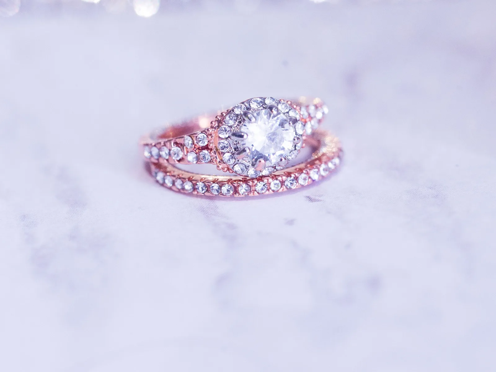 Rose gold diamond ring and matching band resting on a sparkling white surface