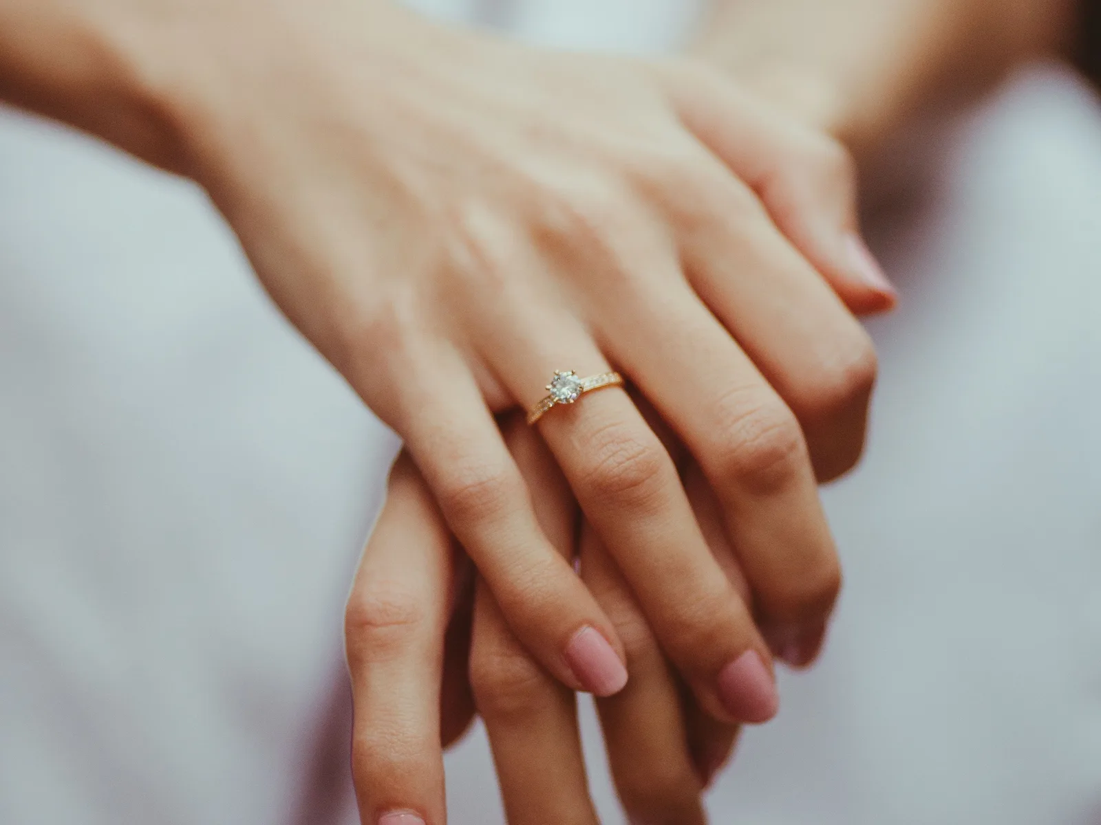 Two hands resting together, one wearing a slim diamond solitaire ring