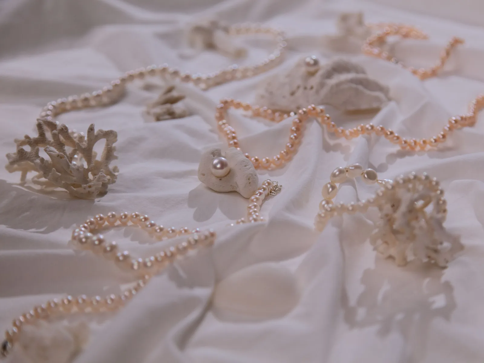 Several strands of small white and blush pearls spread across a soft white linen cloth